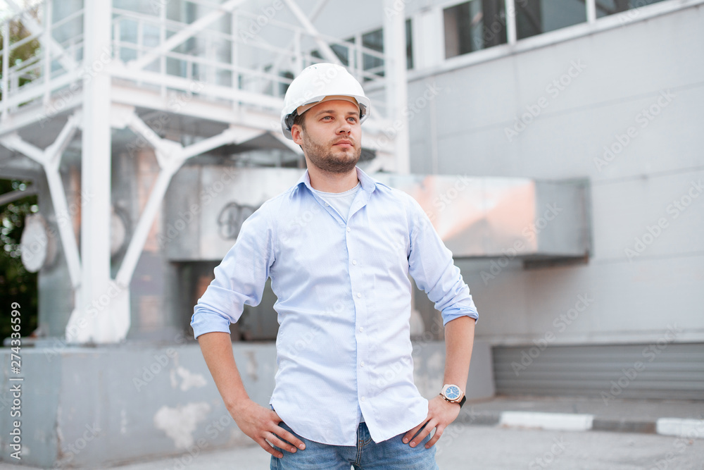 Young handsome male engineer in hardhat standing on the background of water or gas pipes. Concept of boiler station. Pipeline accessories closeup. Heating station manager doing his job outdoor. . Young handsome male engineer in hardhat standing on the background of water or gas pipes. Concept of boiler station. Pipeline accessories closeup. Heating station manager doing his job outdoor. .