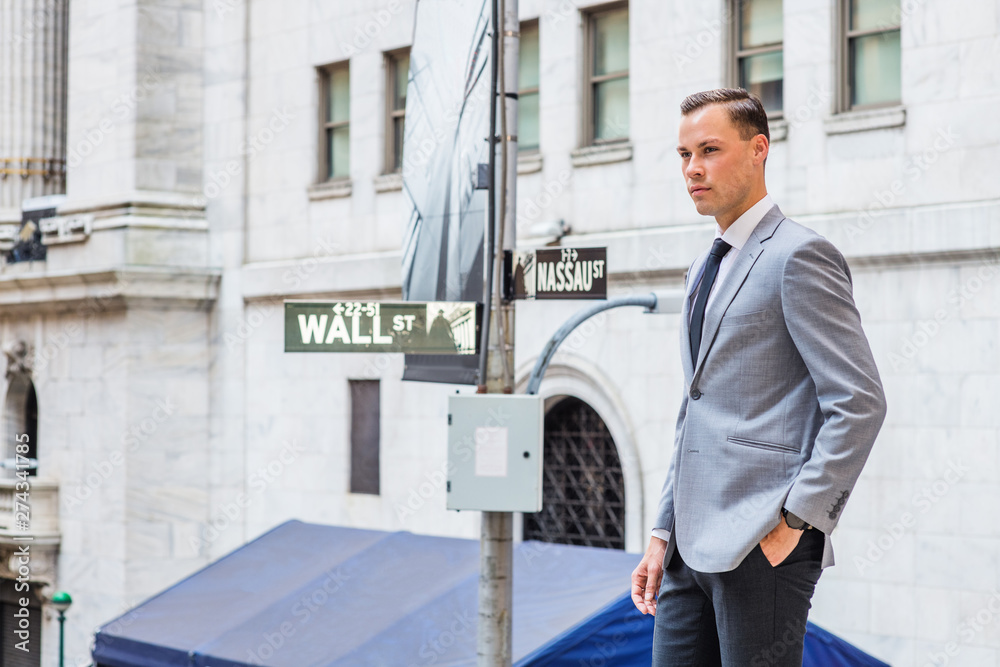 Young Businessman Street Fashion in New York City. Young Man wearing gray  blazer, white undershirt, black tie, standing on street outside office  building by Wall Street sign, looking forward.. foto de Stock |