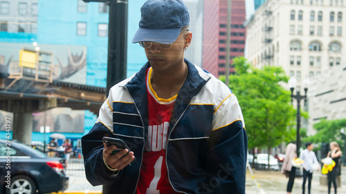 Chicago, IL/United States-June 12th 2019: Young attractive Middle eastern male model is talking on his smart phone smiling while wearing fashion trendy clothes. view from a inside a window pane