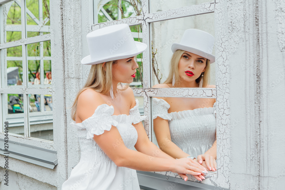 Sexy modern bride in white cylinder hat watching in to mirror window