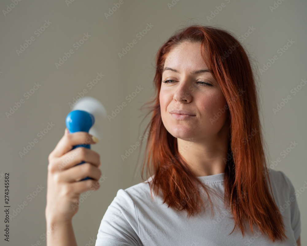 Portrait of a red-haired woman with a pocket fan in her hands. A girl refreshing in the heat of the wind blowing away from a wireless electric device. Enjoy the cool airflow from the air conditioner. Portrait of a red-haired woman with a pocket fan in her hands. A girl refreshing in the heat of the wind blowing away from a wireless electric device. Enjoy the cool airflow from the air conditioner.