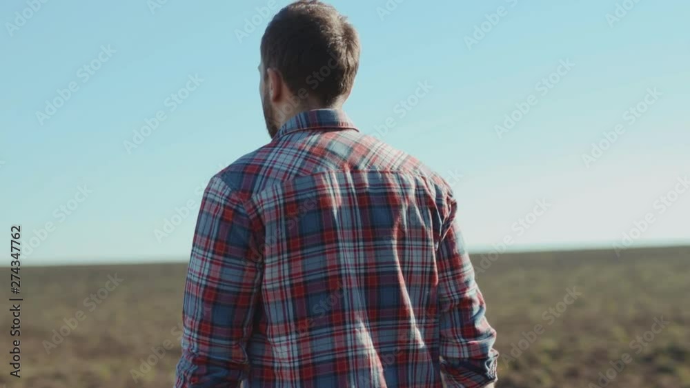 Back view of handsome proud farmer agronomist walking in the large rural field monitoring condition for future harvest in sunny weather in the countryside. Back view of handsome proud farmer agronomist walking in the large rural field monitoring condition for future harvest in sunny weather in the countryside.