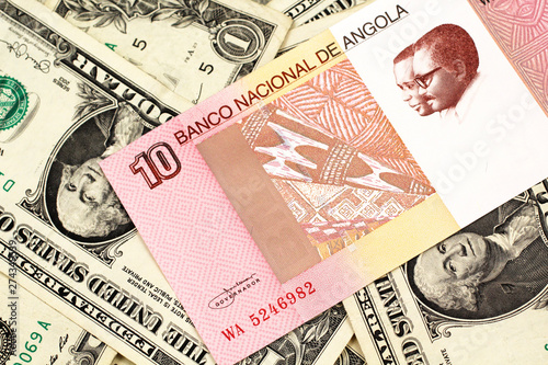 An red and white ten Angolan kwanza bank note on a background of American one dollar bills