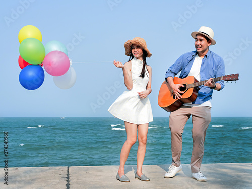 Happy couple playing guitar and holding balloons on the beach, lifestyle concept