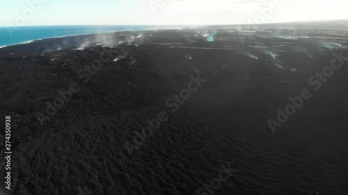 aerial of the massive lava flow that took kapoho subdivision. still steaming months later. the coast in lined with black sand created by hot lava hitting the cold ocean shattering into black sand. photo