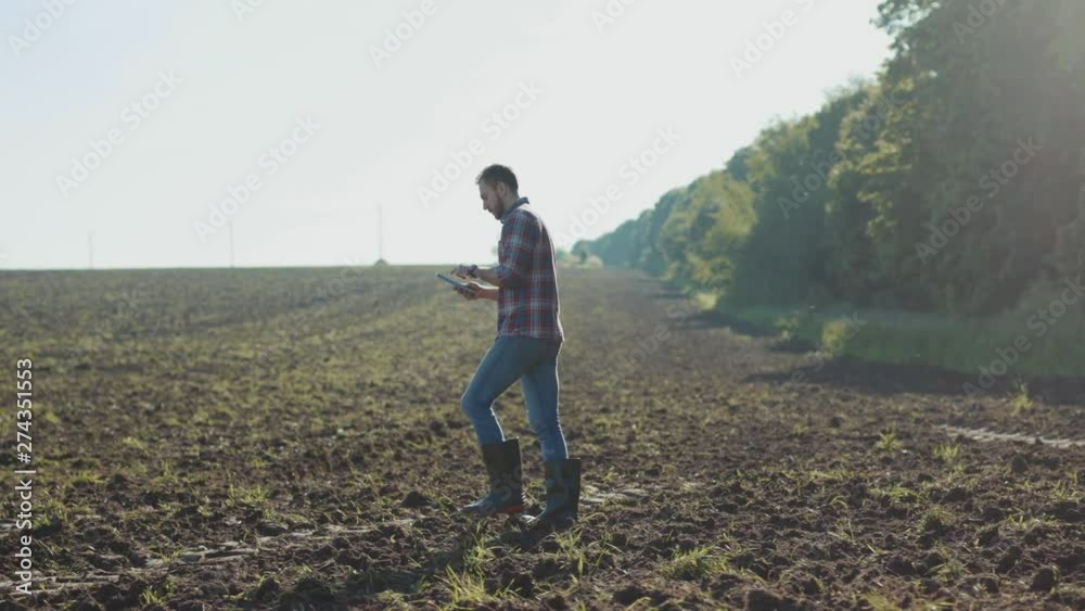 Young man farmer using tablet computer for monitoring a wheat rural field on an industrial farm in early spring. Young man farmer using tablet computer for monitoring a wheat rural field on an industrial farm in early spring.