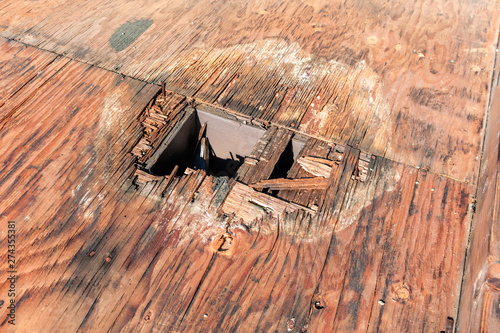Plywood decking damage and water stains from rain water standing, leaking on roof sheathing near downspout hole. Flat roof inspection, repair and replacement project in progress.