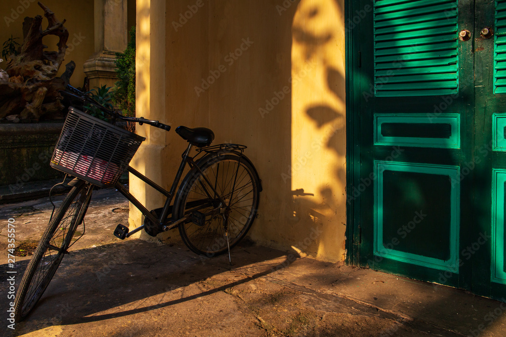 Bicycle in a veranda by a yellow wall with green doors with sun light rays. Shot in Thang Long Citadel in the imperial city, Hanoi, Vietnam. UNESCO World Heritage Site. Bicycle in a veranda by a yellow wall with green doors with sun light rays. Shot in Thang Long Citadel in the imperial city, Hanoi, Vietnam. UNESCO World Heritage Site.