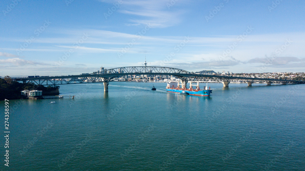 cargo ship travelling pass Auckland Harbour Bridge, with Auckland City as background