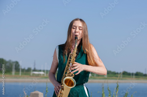 Beautiful brunette plays the saxophone in the park photo