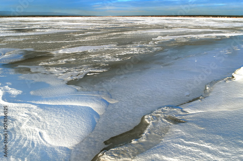 Frozen surface of the river. Snow waves on the ice of a winter pond.