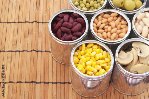 Preserved food on bamboo mat background.Canned green peas, beans, corn, olives and mushrooms in tin cans. 