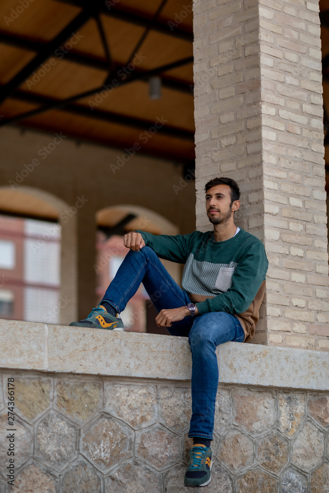 Portrait of a young man with beard and casual clothes sitting in an urban park Portrait of a young man with beard and casual clothes sitting in an urban park
