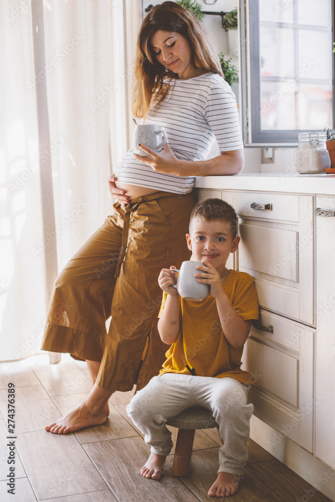 Pregnant mom with kid drinking tea together in the kitchen Pregnant mom with kid drinking tea together in the kitchen