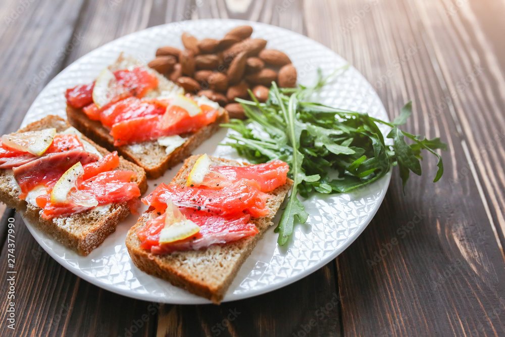 Wholemeal bread with salmon on white plate. Arugula and almond with lemon. Healthy sandwiches. Omega-3 for snack. Proper nutrition. Sport food.