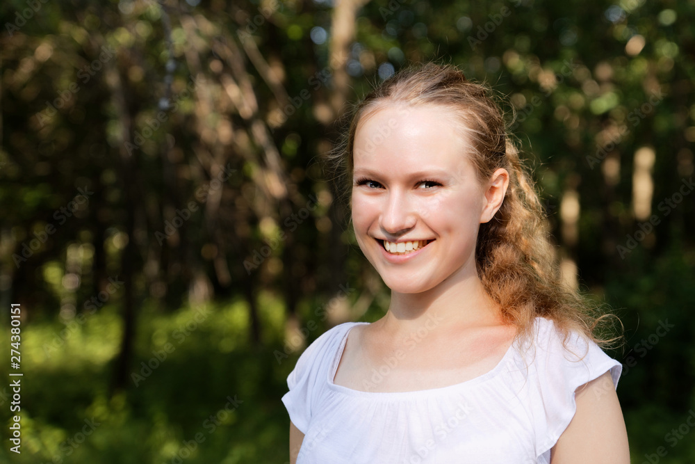 Closeup portrait of a young longhair girl in bright sunlight against blurred dark background of forest or park Closeup portrait of a young longhair girl in bright sunlight against blurred dark background of forest or park