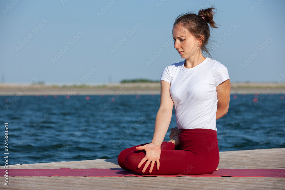 Young woman exercising yoga pose by the lake shore at sunset, girl in headstand yoga pose. People travel relaxation concept.