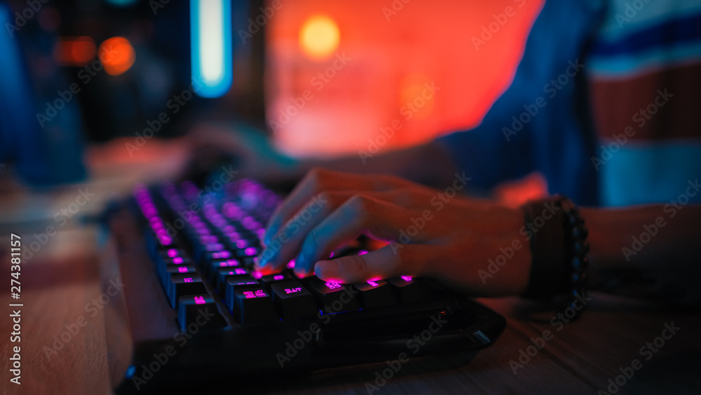 Close Up Hands Shot Showing a Gamer Pushing the Keyboard Buttons while Playing an Online Video Game. Keyboard Led Lights. Gamer is Wearing a Bracelet. Room is Dark. Close Up Hands Shot Showing a Gamer Pushing the Keyboard Buttons while Playing an Online Video Game. Keyboard Led Lights. Gamer is Wearing a Bracelet. Room is Dark.