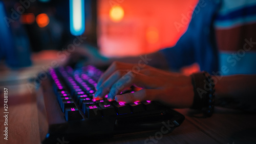 Close Up Hands Shot Showing a Gamer Pushing the Keyboard Buttons while Playing an Online Video Game. Keyboard Led Lights. Gamer is Wearing a Bracelet. Room is Dark.
