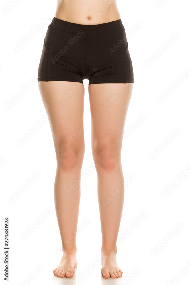 Female barefoot legs in black sport shorts on white background Female barefoot legs in black sport shorts on white background