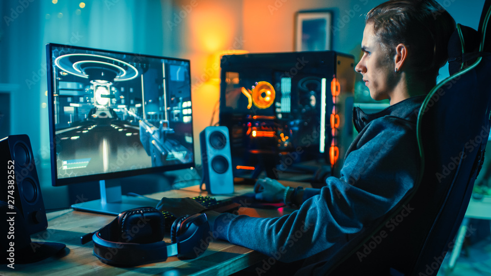 Cheerful Gamer Playing First-Person Shooter Online Video Game on His Powerful Personal Computer. Room and PC have Colorful Neon Led Lights. Cozy Evening at Home.