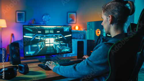 Back Shot of a Gamer Playing First-Person Shooter Online Video Game on His Powerful Personal Computer. Room and PC have Warm Colorful Neon Led Lights. Cozy Evening at Home.