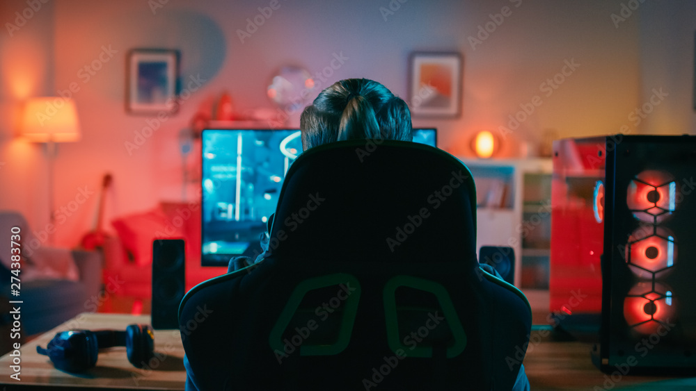 Back Shot of a Gamer Playing in First-Person Shooter Online Video Game on  His Powerful Personal Computer. Room and PC have Colorful Neon Led Lights.  Cozy Evening at Home. Stock Photo