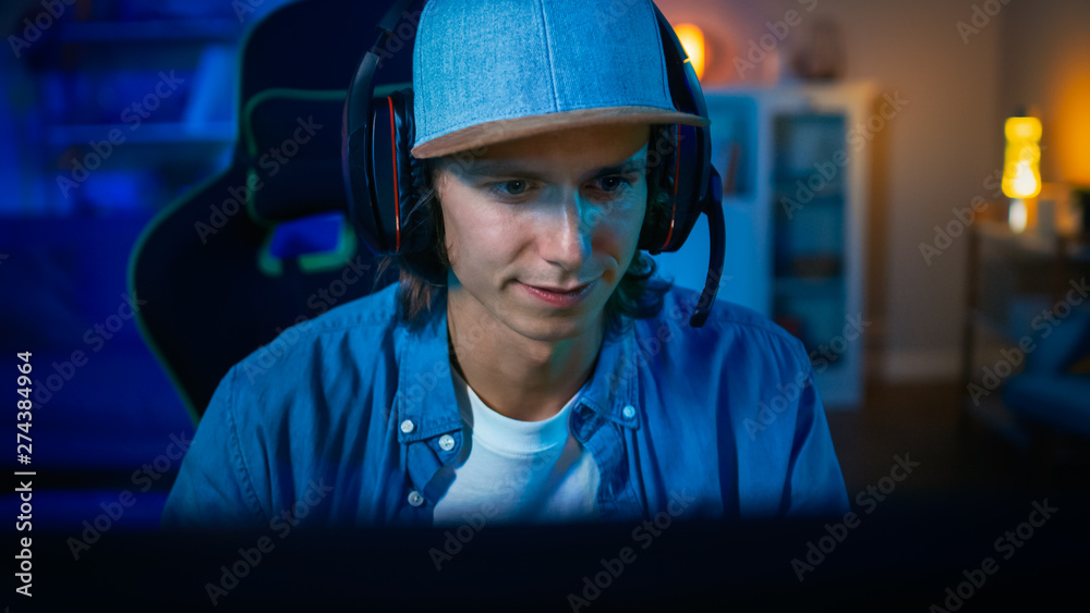 Popular Gamer is Playing Online Video Game on His Personal Computer. Room and PC have Colorful Warm Neon Led Lights. Young Man is Wearing Earphones with a Microphone. Cozy Evening at Home. Popular Gamer is Playing Online Video Game on His Personal Computer. Room and PC have Colorful Warm Neon Led Lights. Young Man is Wearing Earphones with a Microphone. Cozy Evening at Home.
