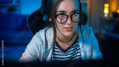 Excited and Pretty Gamer Girl in Glasses is Playing Online Video Game on Her Personal Computer. Room and PC have Colorful Warm Neon Led Lights. Cozy Evening at Home.