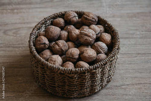 Walnuts in a round wicker basket on a wooden background. Top view.
