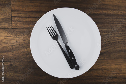 Empty white plate  spoon and knife isolated on wooden background. diet concept.