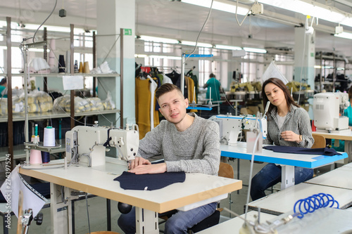 close up photo of a young man and other seamstresses sewing with sewing machine in a factory