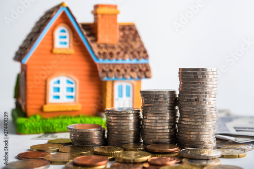step of coins stacks on table with house model background, money saving and investment concept 