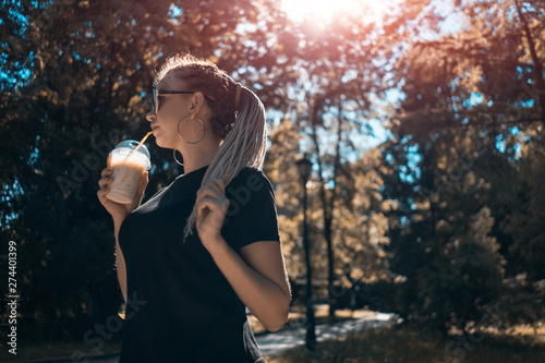 young beautiful braided female drinking milkshake with caramel in sunny park