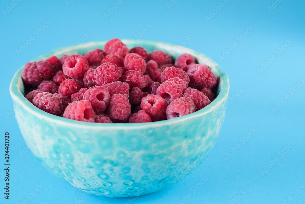 Close up view on ripe fresh raspberry bowl on the blue background Close up view on ripe fresh raspberry bowl on the blue background
