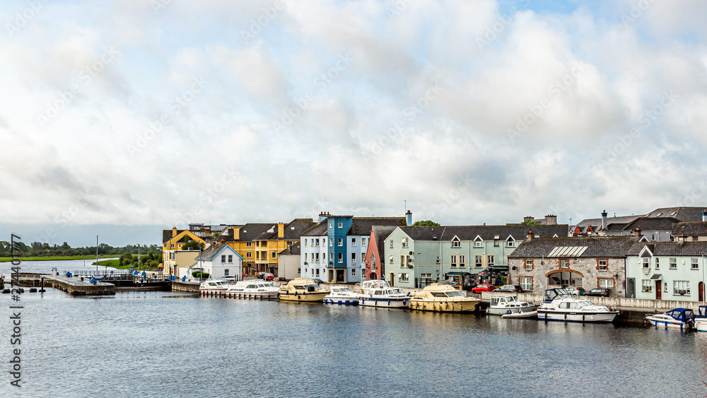 River Shannon with its calm waters with boats moored on the shore at the docks, picturesque houses, relaxed and cloudy day covered by dense clouds in the town of Athlone, County Westmeath, Ireland