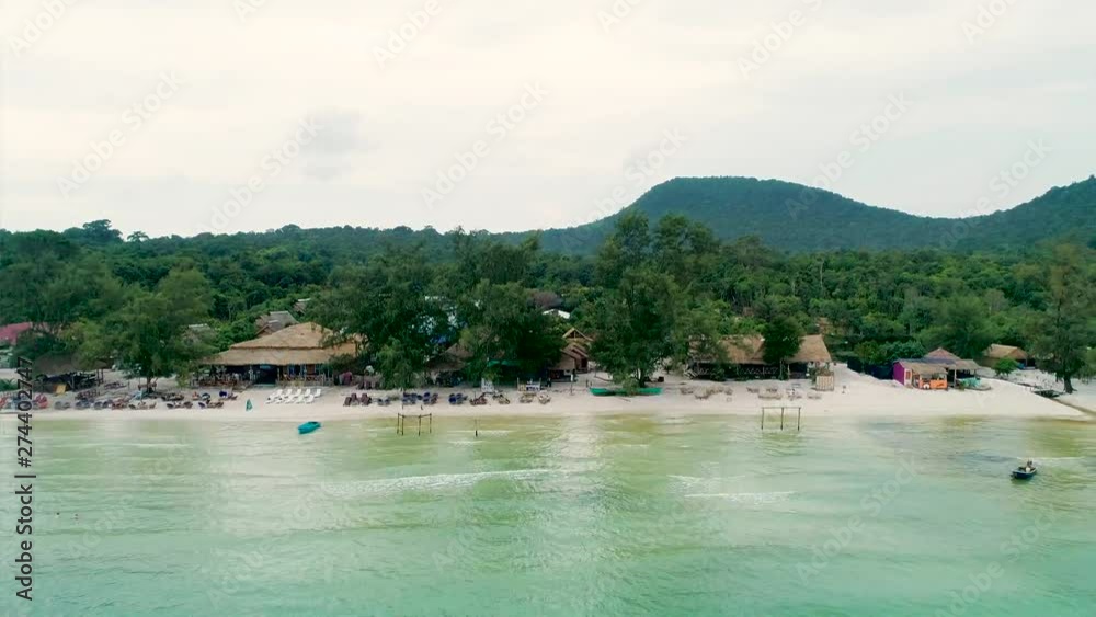 Aerial view of wild beach with white sand, cottages, straw huts, bungalows. Forest and mountain in background. Koh Rong Smaller, Cambodia. Royalty high quality stock footage. flying along coastline.