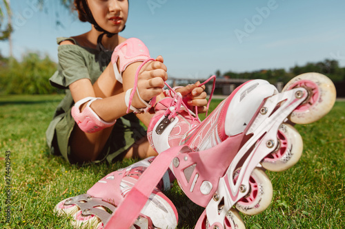 Εκτύπωση καμβά Teenage girl in a helmet learns to ride on roller skates holding a balance or rollerblading and spin at the city's street in sunny summer day