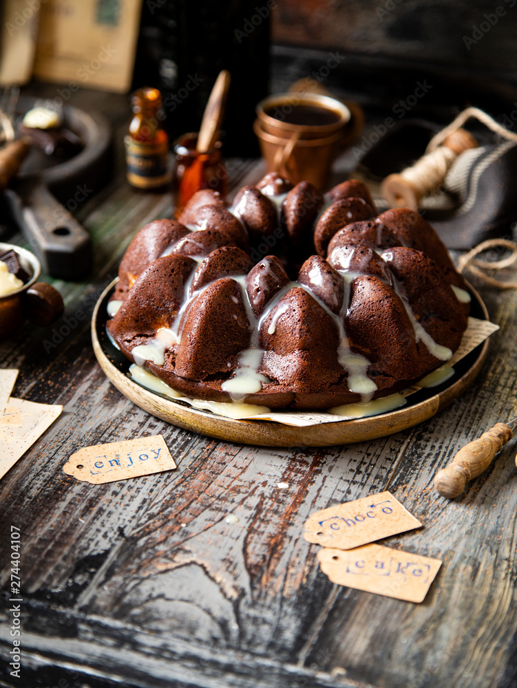 Delicious homemade chocolate bundt cake on wooden plate stands on rustic table Delicious homemade chocolate bundt cake on wooden plate stands on rustic table