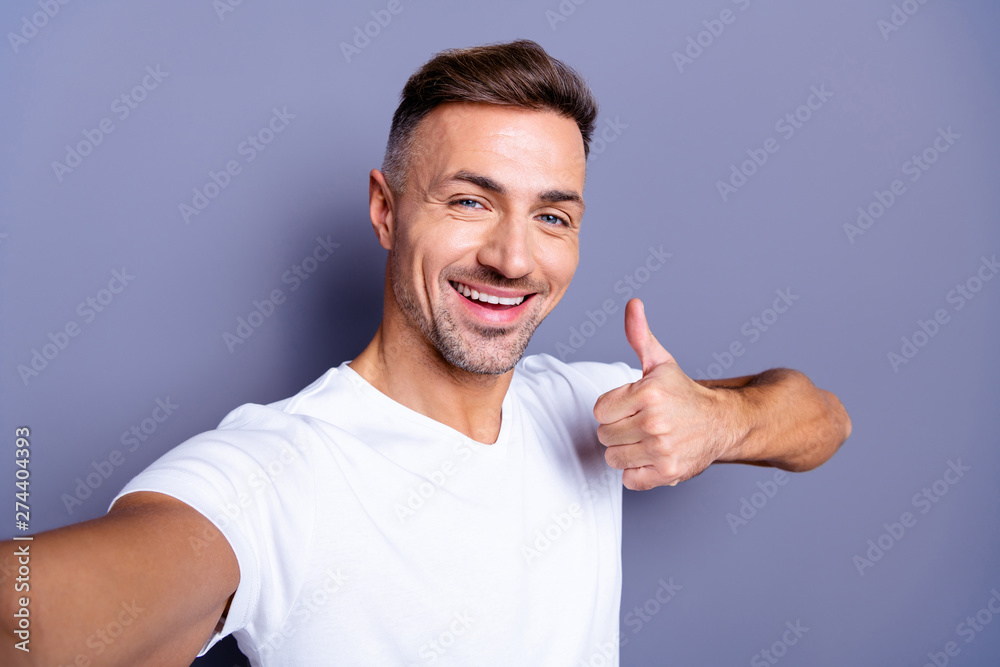 Close up photo amazing positive he him his middle age macho perfect appearance easy-going make take selfies hand arm thumb up symbol toothy mouth wear casual white t-shirt isolated grey background Close up photo amazing positive he him his middle age macho perfect appearance easy-going make take selfies hand arm thumb up symbol toothy mouth wear casual white t-shirt isolated grey background