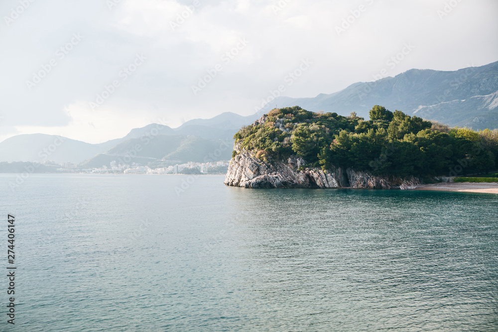 View of the natural landscape. Sea, rocky shore with trees off the coast of Montenegro. In the distance near the mountains is the city of Budva.
