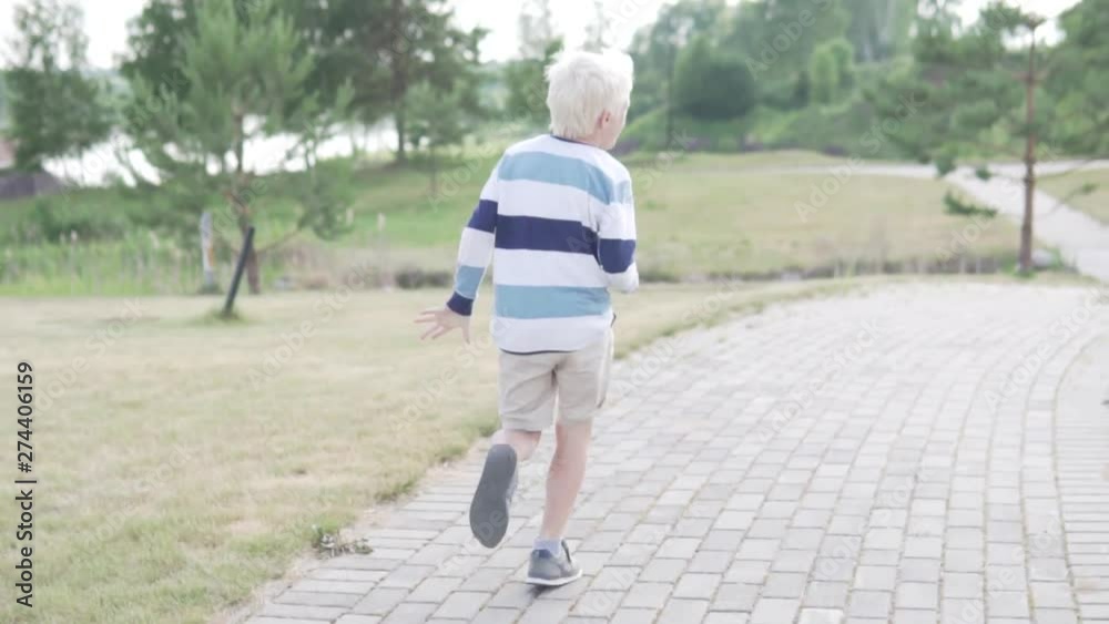 A handsome blond boy is running through the park. Child jogging in the summer park A handsome blond boy is running through the park. Child jogging in the summer park