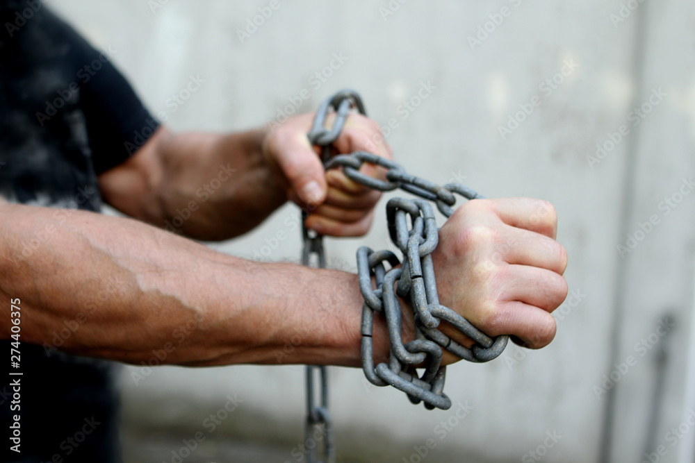 men's hands wrapped in a large iron chain, trying to break them, the concept of bondage, struggle, save space, close-up