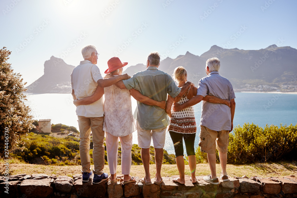 Fototapeta premium Rear View Of Senior Friends Visiting Tourist Landmark On Group Vacation Standing On Wall