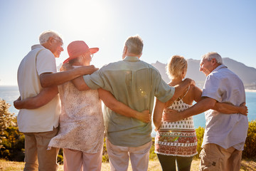 Rear View Of Senior Friends Visiting Tourist Landmark On Group Vacation Standing On Wall