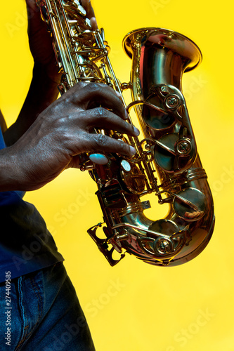 Photography Young african-american jazz musician playing the saxophone on yellow studio background in trendy neon light