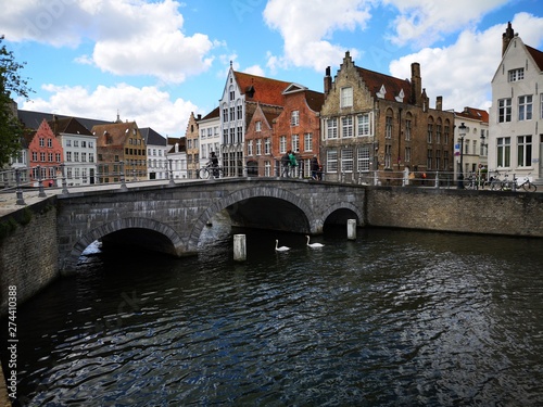 Walkers on a bridge, swans on a canal and Bruges architecture in the background