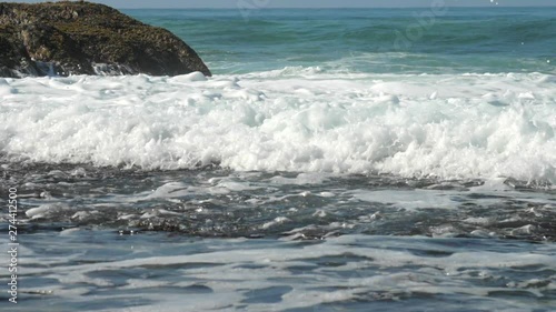 beautiful ocean waves foam near brown rock against blue endless water slow motion. Concept endulf low-lying areas and global warming photo