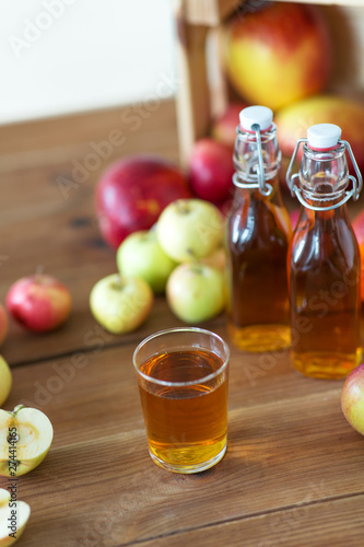 fruits, food and harvest concept - glass and bottles of apple juice or cider on wooden table