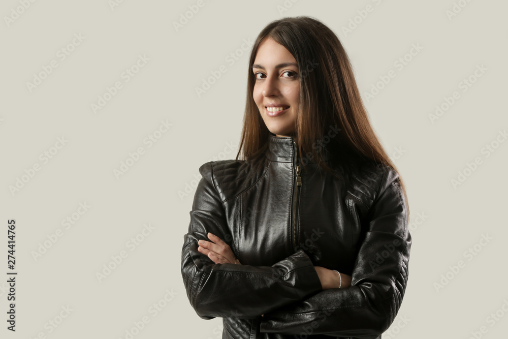 Studio portrait of young smiling brunette in the black leather jacket, arms crossed Studio portrait of young smiling brunette in the black leather jacket, arms crossed